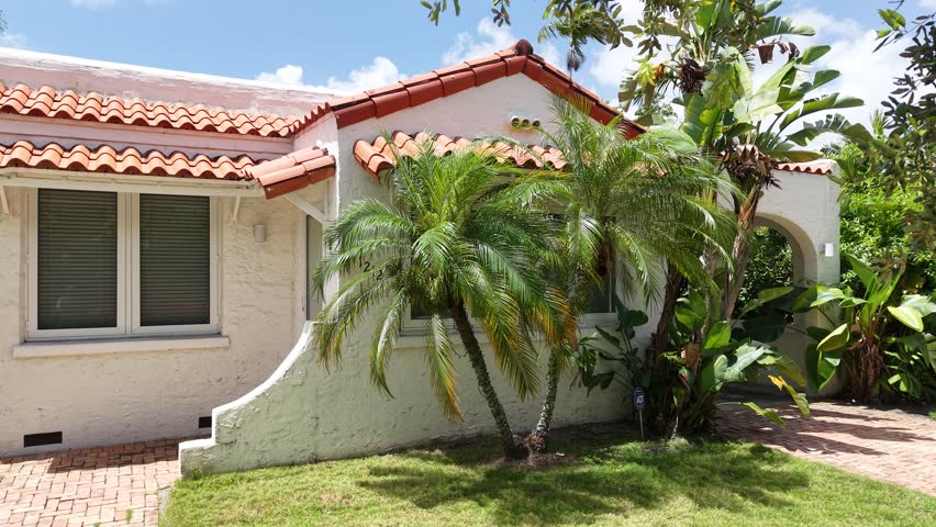 Beautiful single-story Mediterranean-style home in South Florida featuring white stucco walls, a terracotta tile roof, palm trees, and a lush front lawn. Ideal for real estate marketing,  architecture