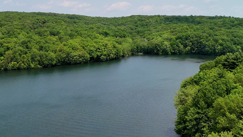 Aerial slow-motion footage of Crescent Lake in the USA, a peaceful lake surrounded by dense forest. Towering trees and vibrant greenery create a natural retreat.