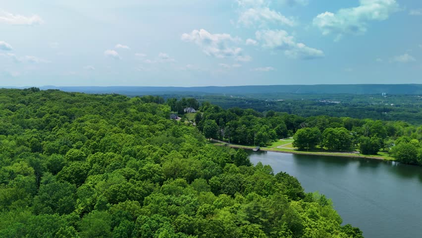 Aerial slow-motion footage of Crescent Lake in Southington, Connecticut, USA. Scenic view of lush green forest, calm water, and recreational area popular for fishing, kayaking, and hiking. 1 minute.