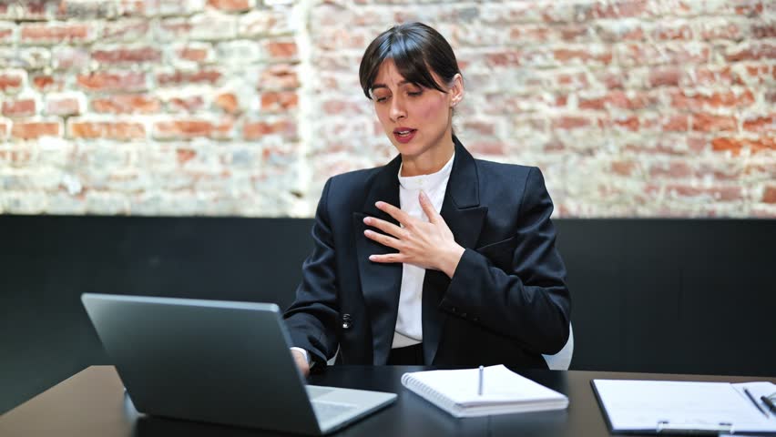 Stressed businesswoman in office suit has panic attack in loft office. Businesswoman in formal wear works on laptop. She feels anxiety and stress.