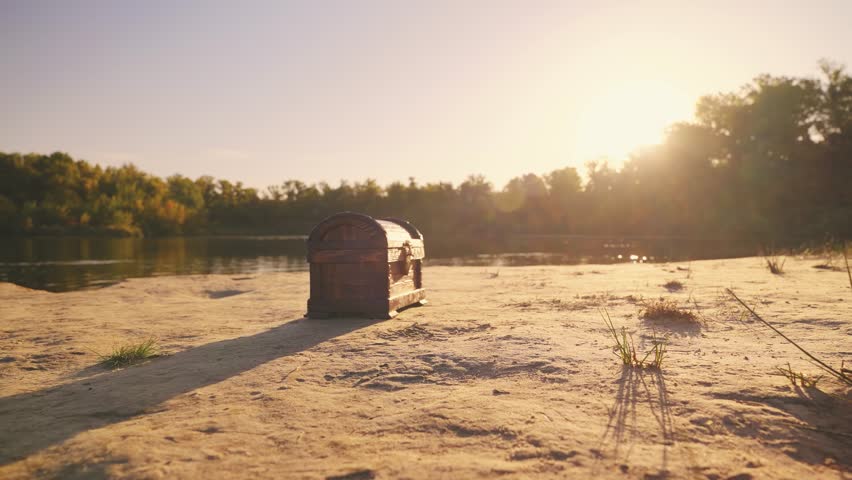 Old style brown chest stands on sand river bank lake sea. Treasure chest wooden box with a lock. Shooting close-up object details fantasy game search for pirate treasure. Nature summer sun light flare