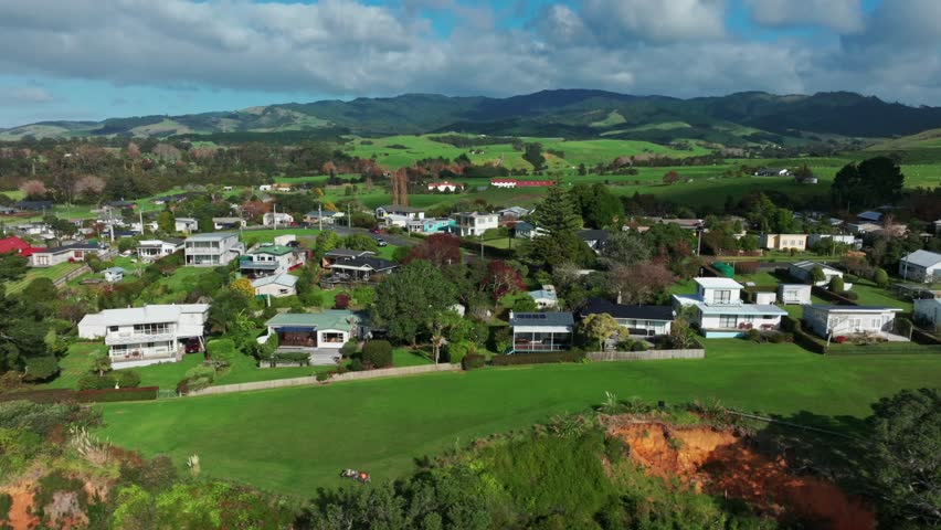 Aerial view of a coastal residential area of Orere Point nestled between green hills and the ocean cliff edge in Auckland, New Zealand