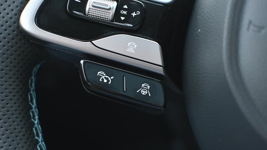 Close-up of modern car steering wheel with adaptive cruise control and lane keeping assist buttons, illustrating advanced vehicle technology.