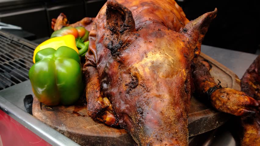 Camera moves along a market meat stall displaying whole roasted piglets with golden brown crispy skin. Traditional pork roasting. Appetizing meat dish ready to serve or sell.