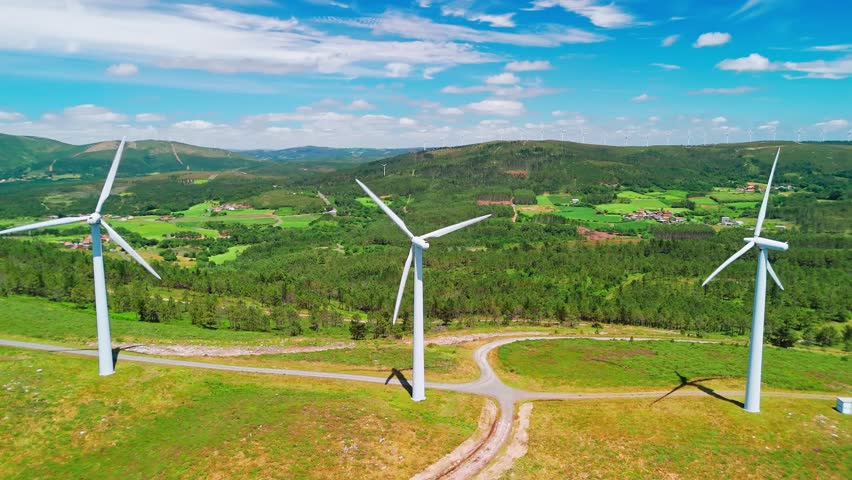 Aerial view of large white wind turbines with spinning blades on top of a mountain. Wind power generating self-sufficient, eco-friendly electricity on a beautiful sunny summer day.