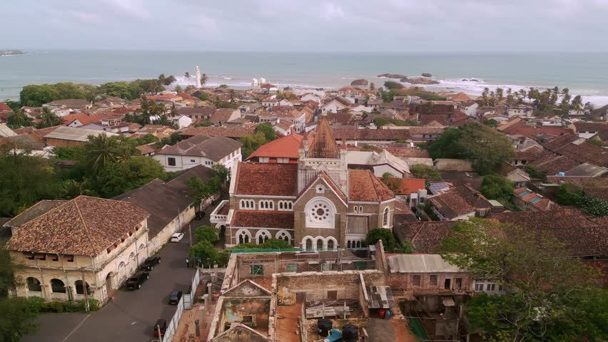 Aerial footage of Galle Fort in Sri Lanka shows colonial-era church architecture and tiled rooftops near the beach, perfect for tourism promos, travel ads, or heritage documentaries.