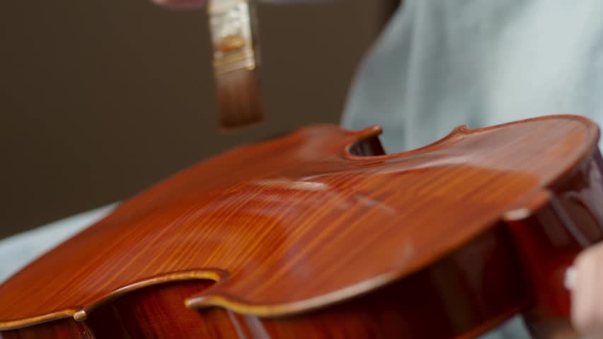 Master violin maker artisan varnishing handmade classical violin with self produced natural paint, with precise brush strokes and focus, slow motion footage