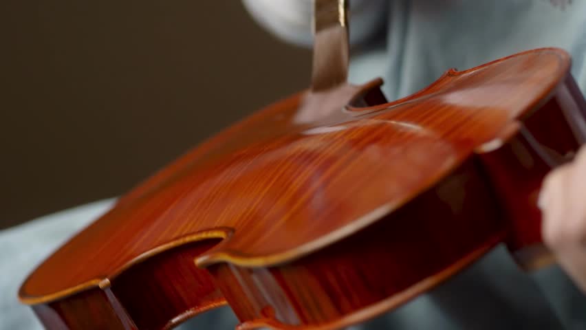 Master violin maker artisan varnishing handmade classical violin with self produced natural paint, with precise brush strokes and focus, slow motion footage