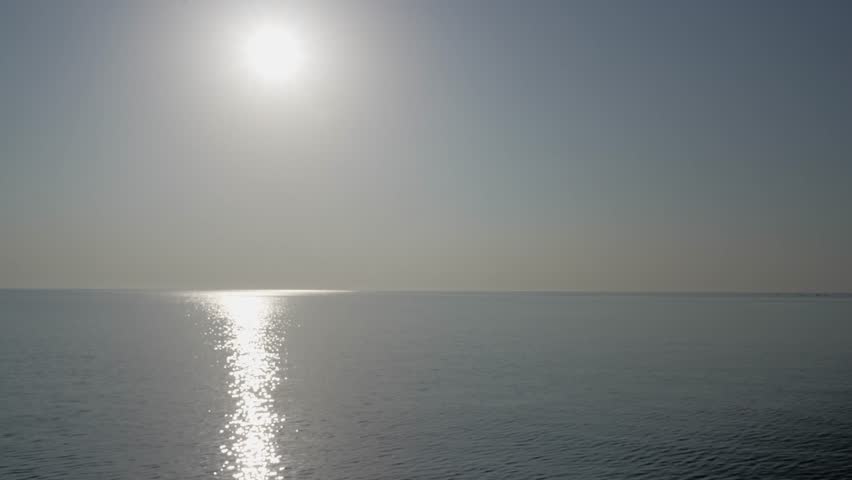 4K 60fps ProRes stock footage of the Sardinian sea at dawn. Hazy white sky, smooth water, and a glowing sun reflection create a calm, spiritual, minimalistic background