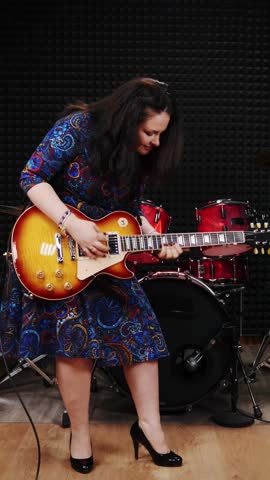 Young charming woman is performing song in professional recording studio and playing guitar. Female musician playing on electric guitar. Vertical video