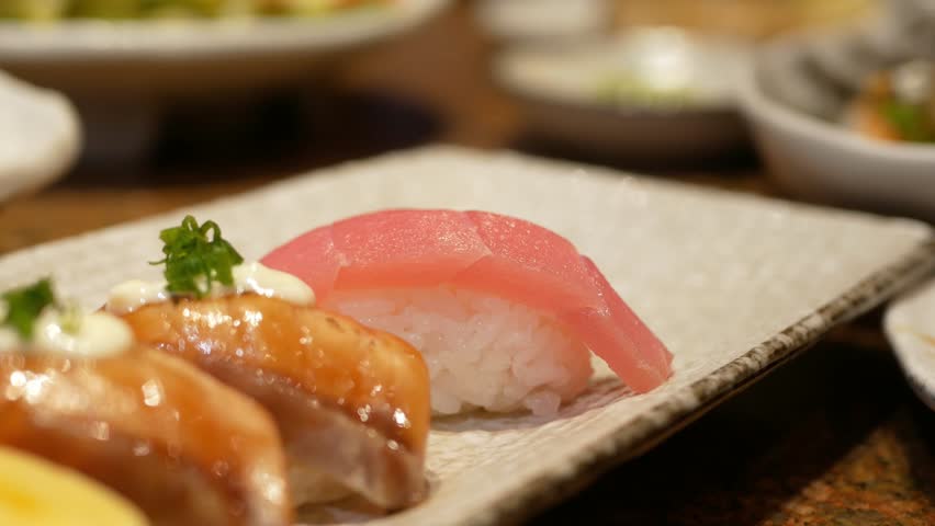 close up selective focus to a plate of japanese food with sushi while hand using chopstick to pick up a sushi from a plate in lunch time. modern traditional japanese food.