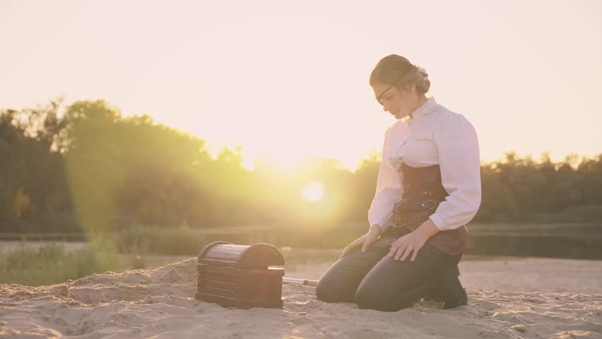 person hands open touching treasure chest gold coins glowing shiny in sun light magic flare. Fantasy woman pirate finds treasure wooden box old style full of rich jewelry. Nature sand desert island 4k