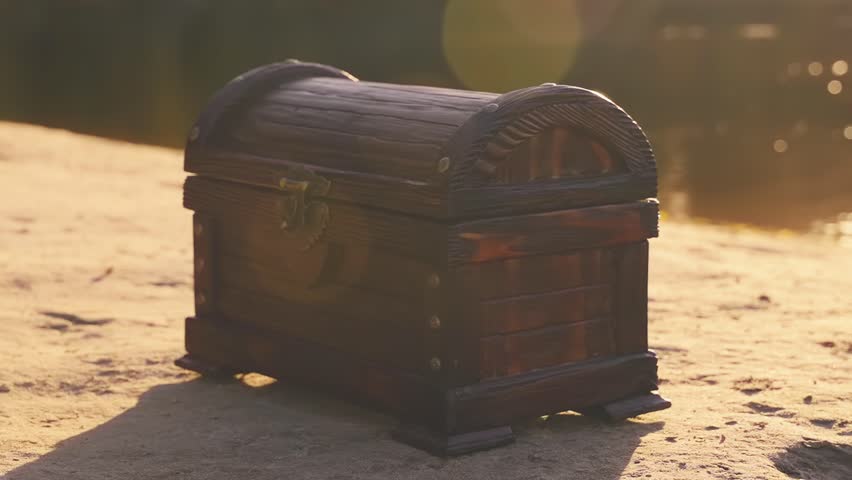 Old style brown chest stands on sand river bank lake sea. Treasure chest wooden box with a lock. Shooting close-up object details fantasy game search for pirate treasure. Nature summer sun light flare