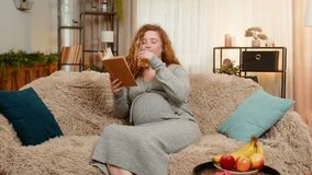 Pregnant young woman sits on home sofa, sipping fresh orange juice and reading pregnancy book with relaxed expression. Girl enjoys happy moment, reflecting on future motherhood and gentle lifestyle - Powered by Shutterstock - Get 15% off with code: PIKWIZARD15