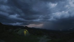 Dramatic zoom in timelapse of couple camping in tent top mountain thunderstorm brews, glowing shelter against dark clouds and lightning in distant horizon.Concept hikers under lightning sky isolated - Powered by Shutterstock - Get 15% off with code: PIKWIZARD15
