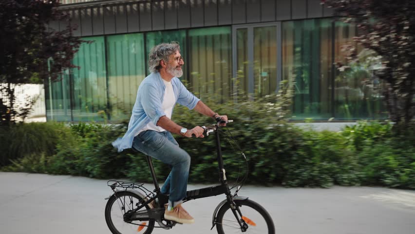 Happy active senior man cycling on city street riding foldable electric bicycle