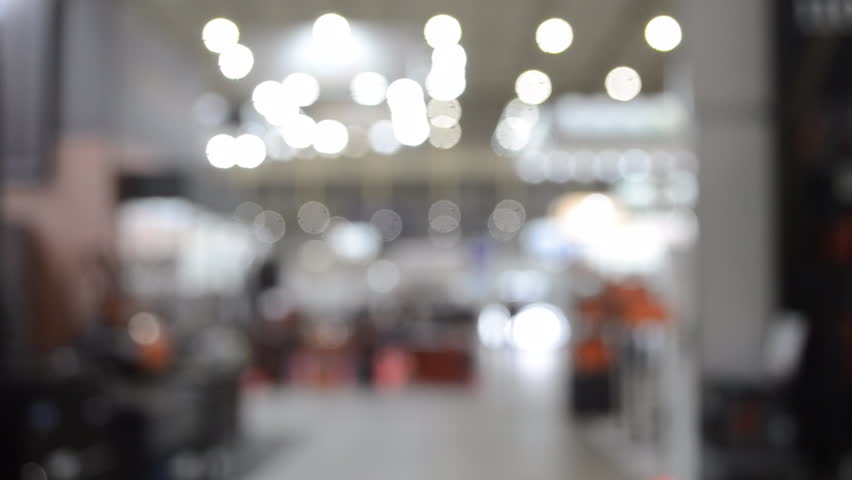People walking in building. Building with walls, floor, ceiling illuminated lamps. Silhouettes of people indoors. Many people walking. Men and women in tall hall. Exhibition center. Blurred background