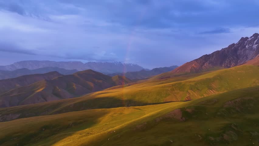 A vibrant rainbow arcs over a lush green mountain valley with a winding river, under a dramatic sky at sunset or sunrise