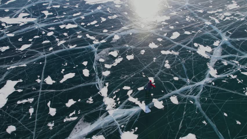 Skater gliding over cracked ice surface of lake Baikal in Russia under bright sunlight.