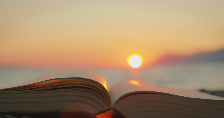 An open book on a beach at sunset with a calm sea in summer