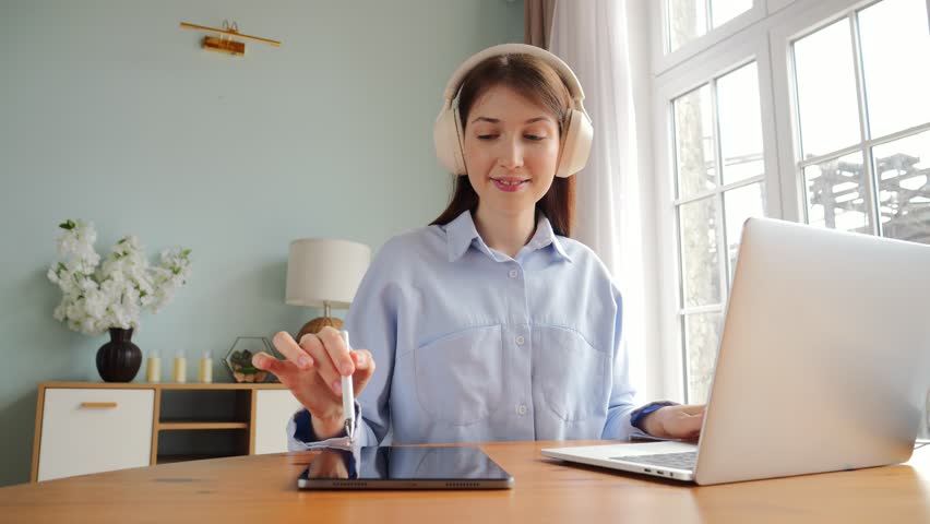 Engaging in a Productive Work Session at Home With a Tablet and Laptop While Wearing Headphones for a Focused Experience