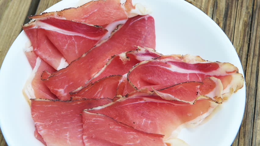 Speck cured pork meat prosciutto thin sliced food, slices on white plate at wooden kitchen table from Italy South Tyrol macro closeup