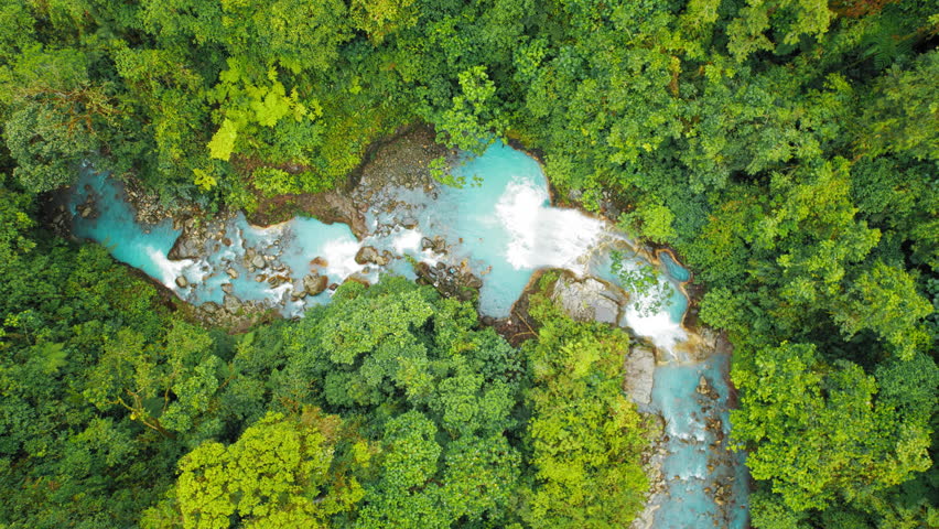 Aerial view of vivid blue waterfall surrounded by lush rainforest in Costa Rica jungle