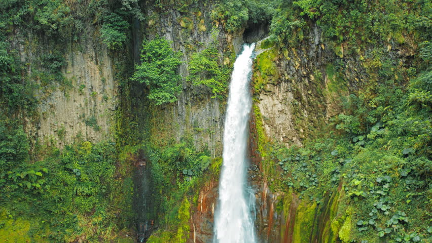 Waterfall del Toro crashing into rocky pool in green mossy canyon in Costa Rica