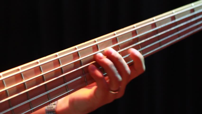 A musician's hand expertly presses strings on a bass guitar fretboard. The detailed close-up highlights skilled finger work and the instrument's design. Perfect for showcasing musical talent and rhyth