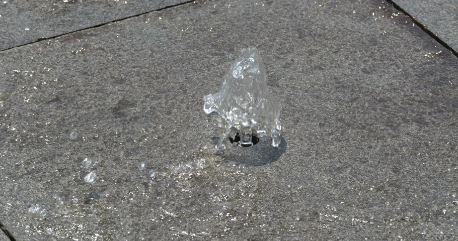 
A small fountain sprays water upwards from a tiled grey surface.