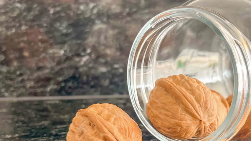 walnuts spilling from a glass jar on a dark surface. A close up shot showing the texture and detail of the nuts and the jar