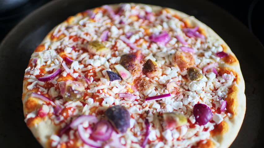 Frozen raw pizza dough crust before baking with goat cheese and red peppers and fig fruit on tomato sauce on baking pan macro closeup of texture