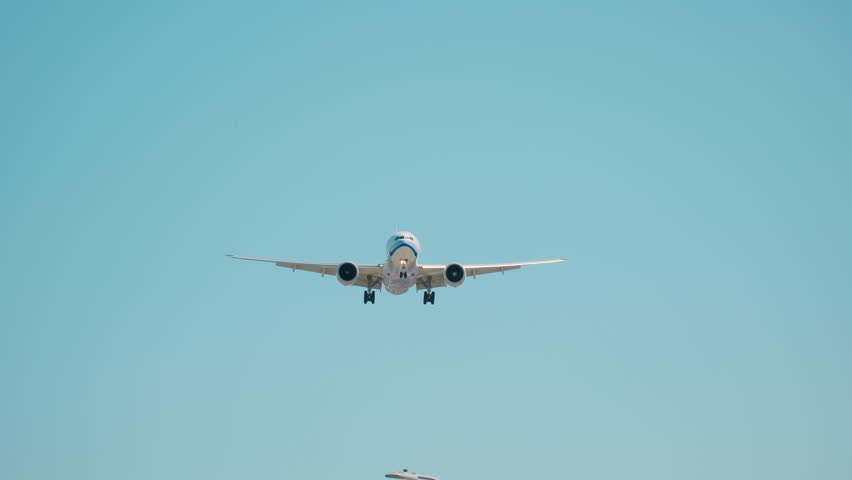 Plane flying over the head, landing at airport with barbed wire on net fence at sunny bright day time. Slow motion footage