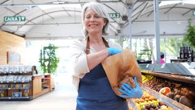 Senior female greengrocer carefully selecting ripe, colorful fruits and filling paper bag while working at local grocery store produce counter with professional care - Powered by Shutterstock - Get 15% off with code: PIKWIZARD15