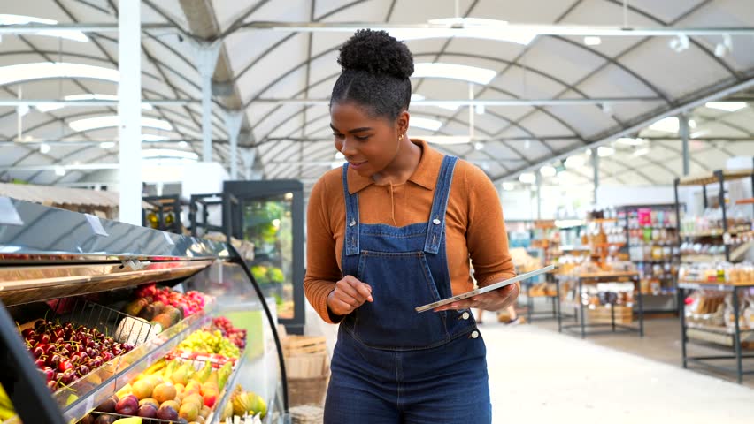 Young african american supermarket employee using digital tablet checking fresh fruits in grocery store