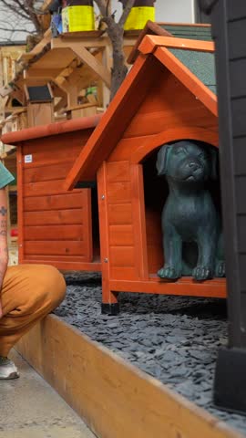 Shop assistant showing a wooden dog house with a puppy statue inside to a customer in a pet shop