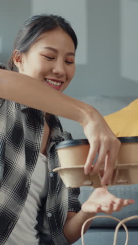 Vertical Screen : Happy asian young attractive couple man and woman sit at new home drink coffee relax and talk smile with carton package box storage to move in new house. Married move home concept.