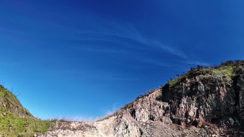 Scenic volcanic crater lake with turquoise water, rocky shores, and sparse trees under a clear blue sky in a natural reserve