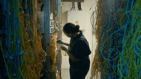 Tilt up side view of female data center specialist inspecting and fixing wires and cables in room - Powered by Shutterstock - Get 15% off with code: PIKWIZARD15