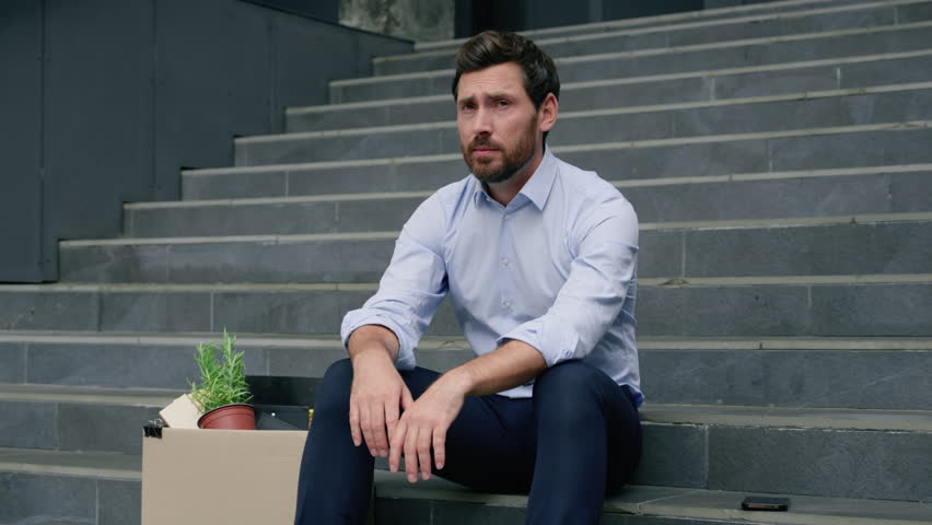 Middle-aged mature businessman business man male employer sad upset sitting on office stairs with packing belongings things office staff dismissed box leaving company unemployment economic crisis