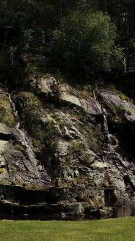 Small natural waterfall running down a rocky hill surrounded by pine trees in Mokra Gora, Serbia. Vertical footage