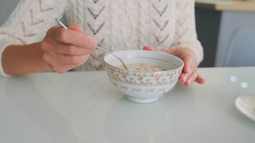 Caucasian woman enjoying healthy breakfast in the kitchen, eating oatmeal. Lady eats sweet vegan cereal bowl. Close up.