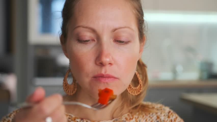 Extreme close-up of a young woman's mouth as she brings a forkful of cooked vegetables peppers and zucchini towards her lips. Healthy eating and the enjoyment of food.