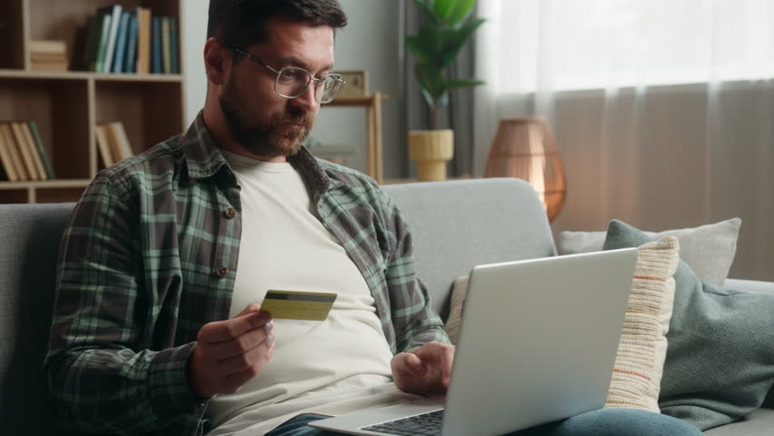 Happy smiling client buyer Caucasian man male guy at home with credit card and laptop computer shopping buying online purchase check money financial account order food delivery payment internet bank
