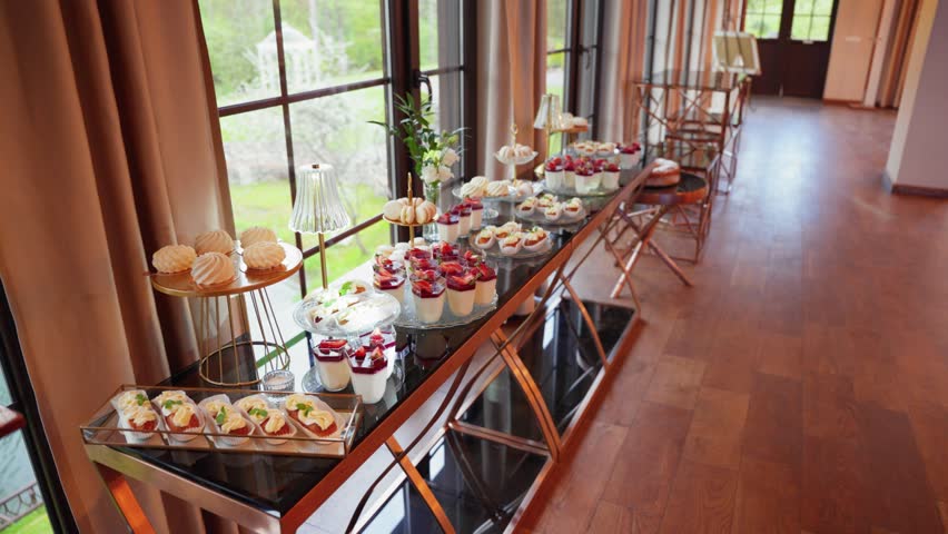 The desserts and cake displayed on glass tables near windows in a wedding venue