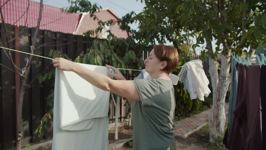 Woman taking dry laundry off clothesline in backyard garden