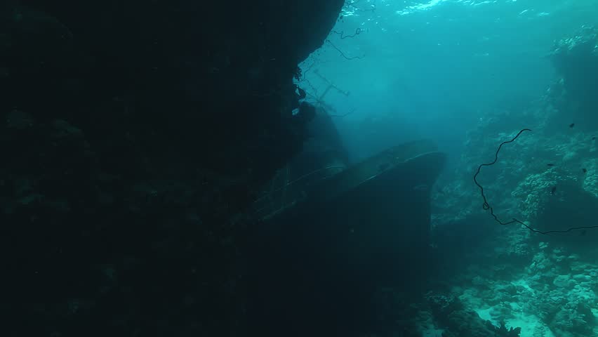An abandoned fishing trawler lies submerged between vertical reef cliffs in the Red Sea. Dark underwater view from mid-range. Check my portfolio for more shipwreck footage.