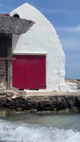 A charming beachside scene at Binibeca Nou with a traditional whitewashed building, a red door, and turquoise waters in the background. 