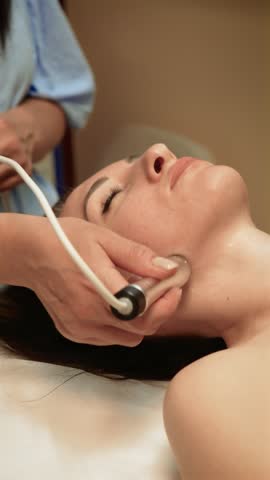 Beauty professional performing Cryotherapy Facial Treatment on chin, vertical orientation. Aesthetic therapist using cold therapy to reduce inflammation and tighten skin. Skincare specialist enhancing