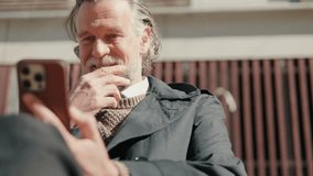 Smiling mature man uses his phone outdoors. He sits on bench and using mobile phone. Senior man using smartphone. - Powered by Shutterstock - Get 15% off with code: PIKWIZARD15